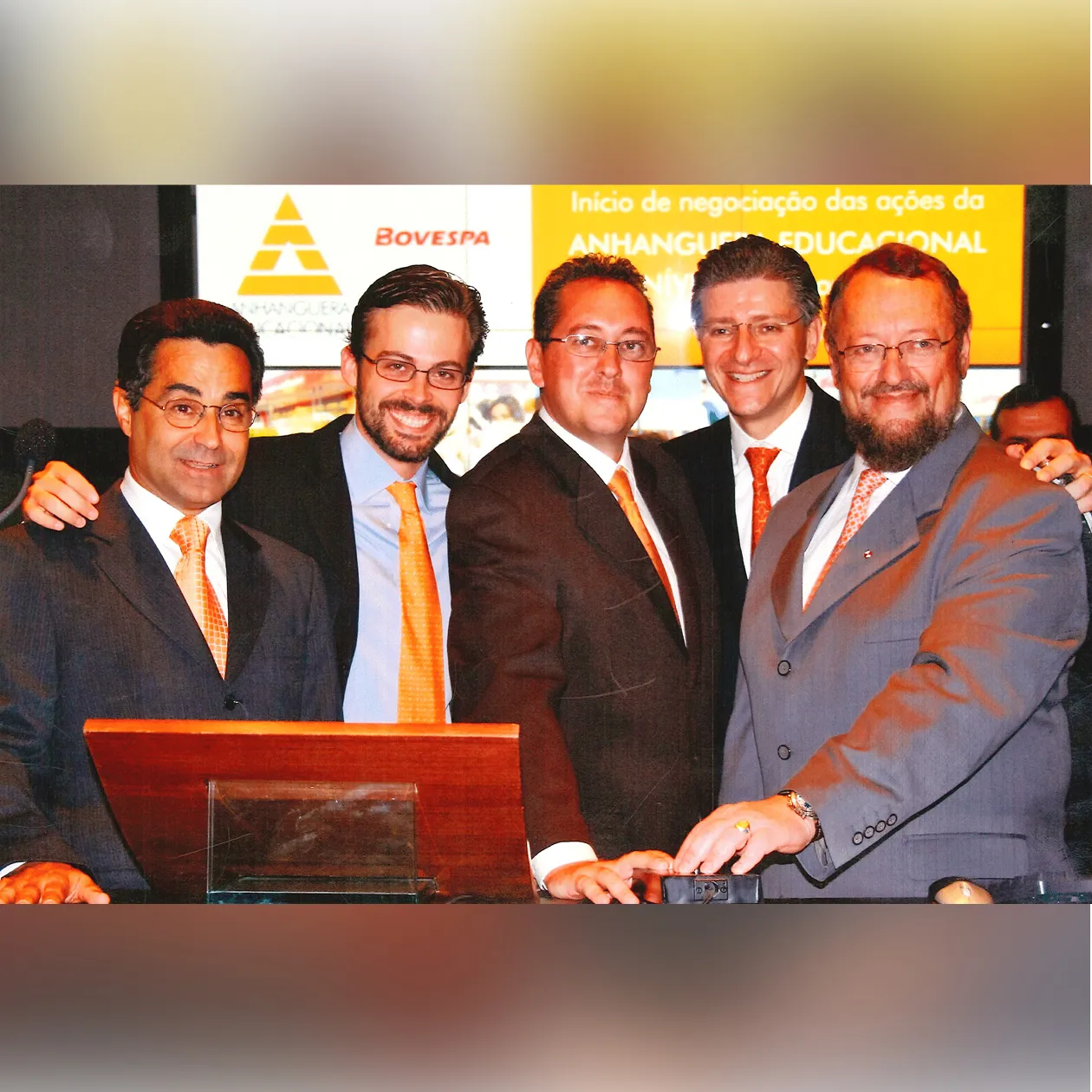 Executivos sorridentes na Bovespa durante o IPO da Anhanguera Educacional, em frente a um painel amarelo